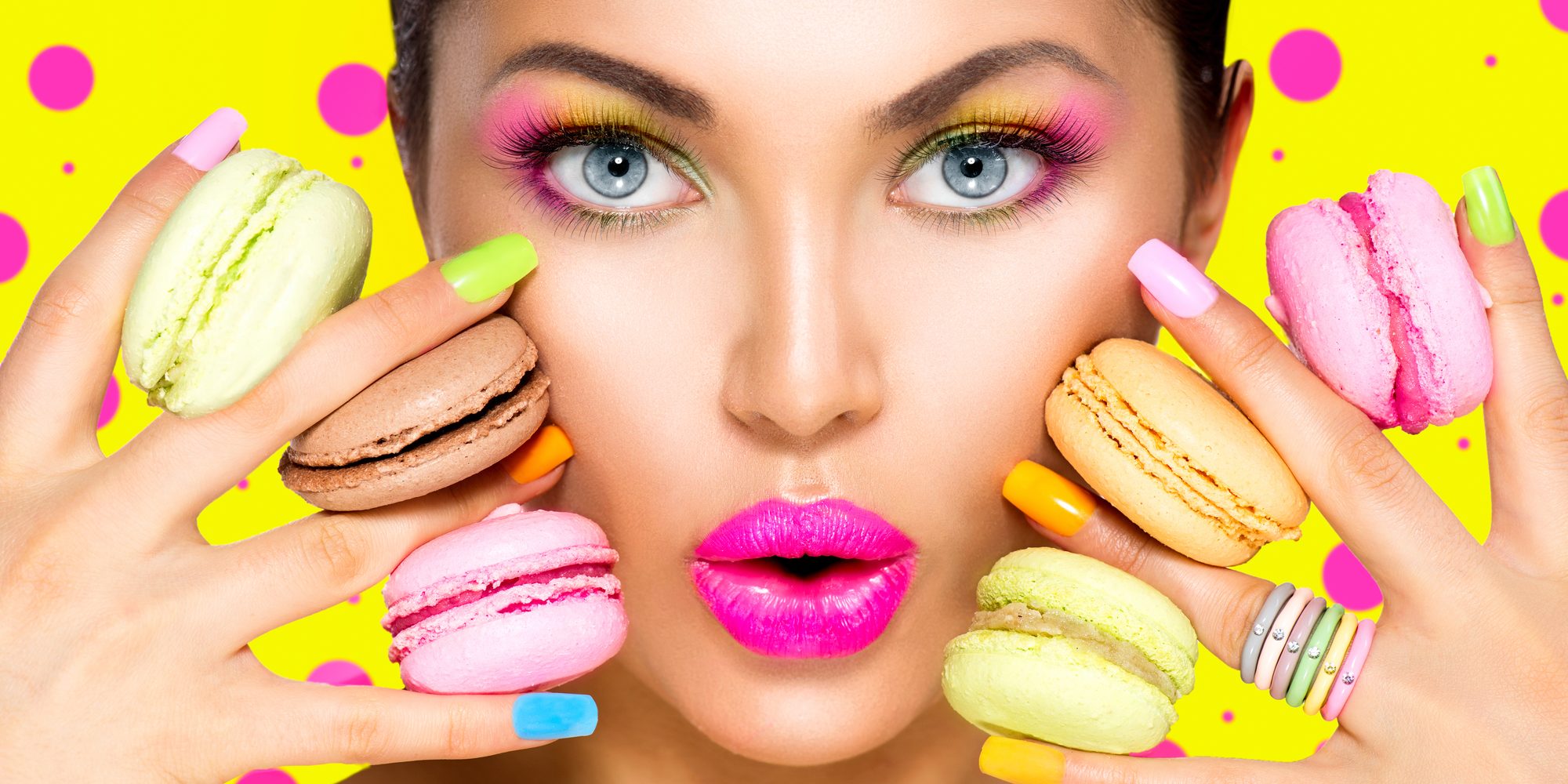 Girl with colorful makeup and manicure taking colorful macaroons